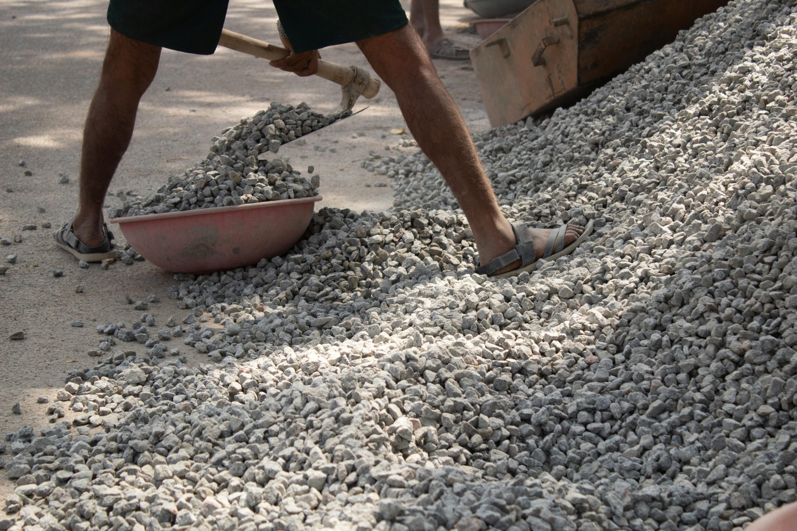 Man using a shovel to move rocks on a construction site in Bengaluru, India.